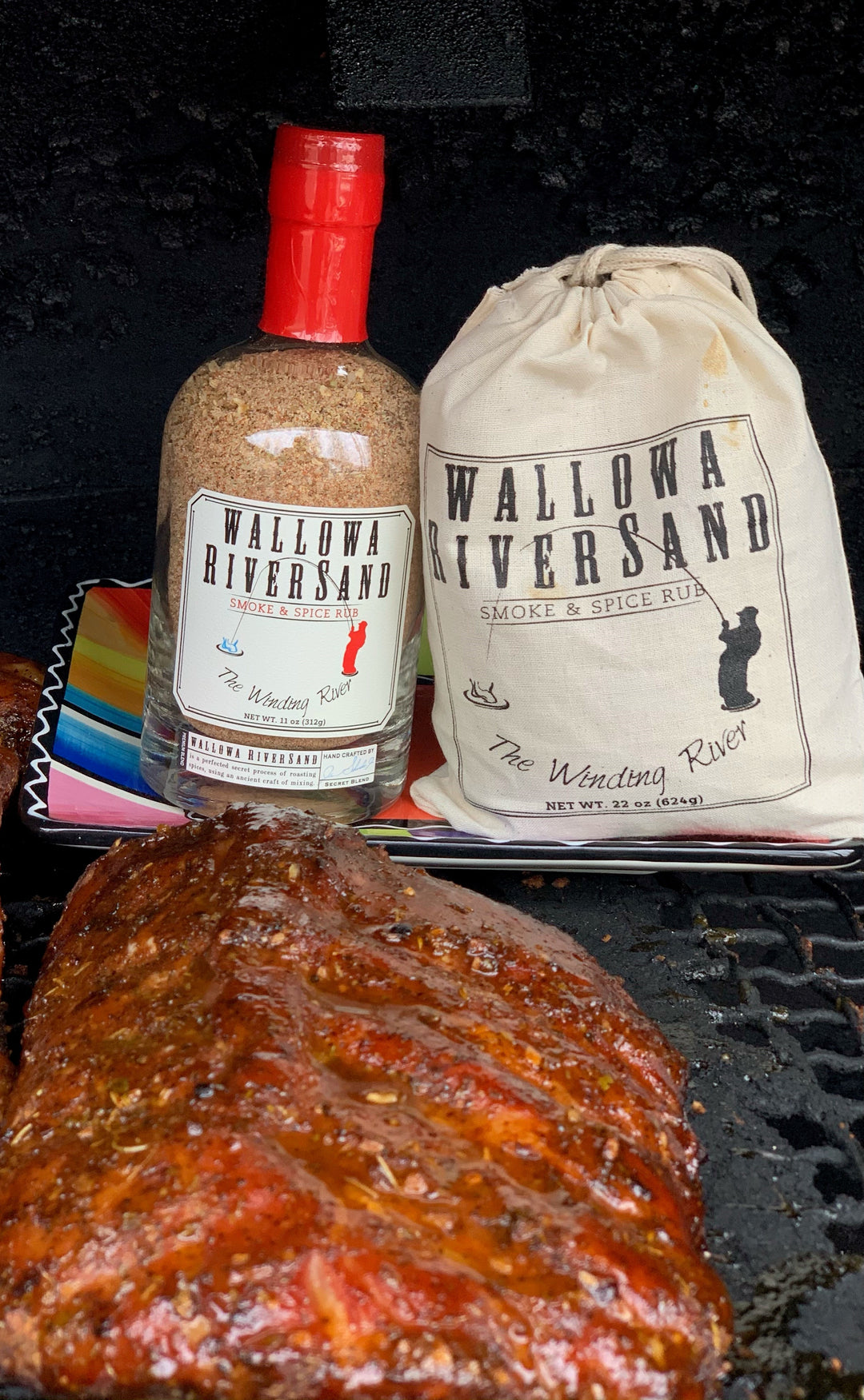BBQ ribs on a barbecue grill with a bottle of Wallowa Riversand and a WRS refill bag